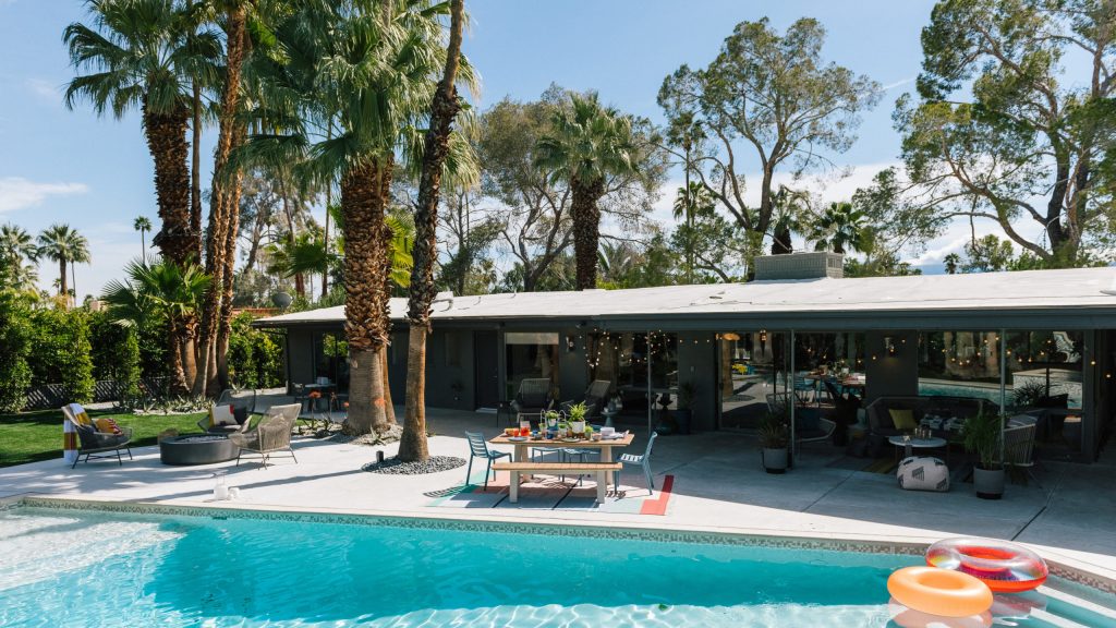 A photo of a pool and house with entertaining furniture and pool floaties. 