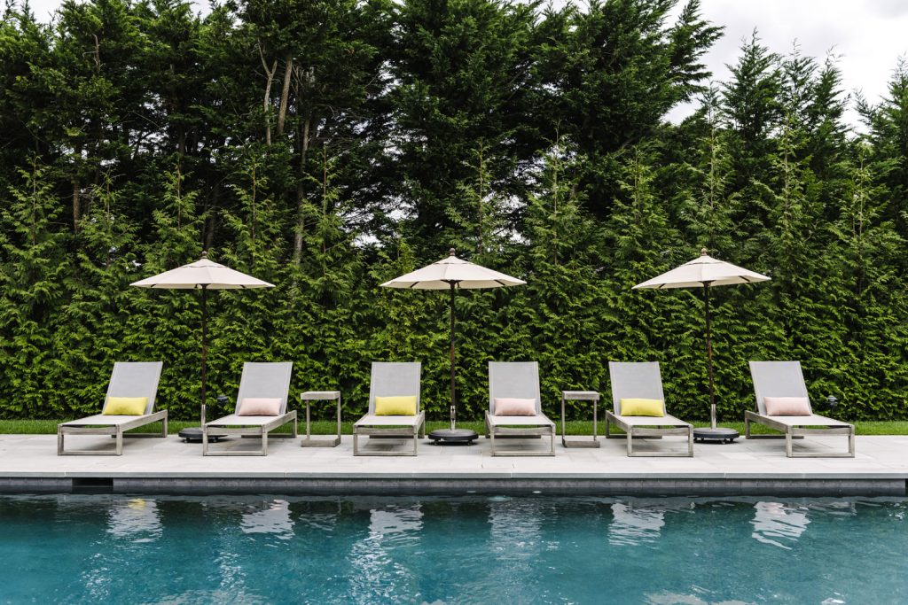 A photo of pool chairs and a pool surrounded by pines. 