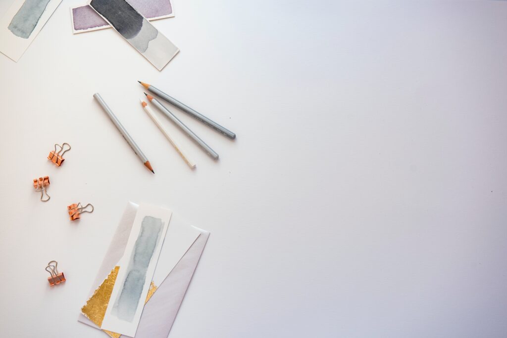 A lilac background with pens, clips and strips of painted papers 