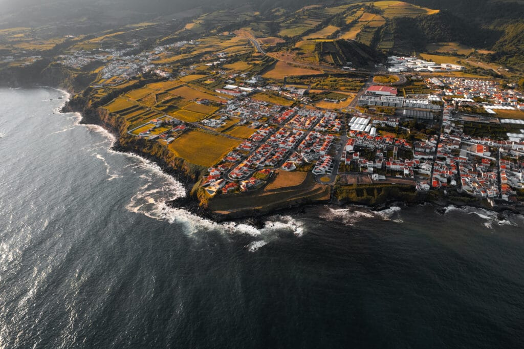 From above drone view of Villa Franca do Campo village with small houses located on shore of Atlantic ocean , with rippling water and foamy waves in summer day in Portugal 